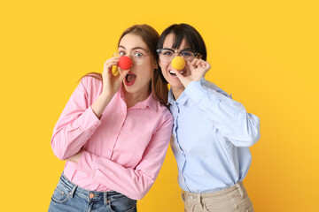Beautiful young shocked women with funny clown noses on yellow background. April Fools Day...