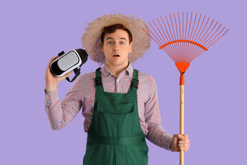 Shocked male farmer with rake and VR glasses on lilac background