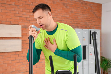 Sporty young man using inhaler on exercise bike in gym