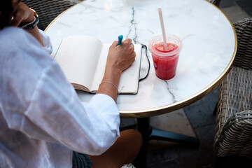 Unrecognizable woman writing on notebook on table outdoors.