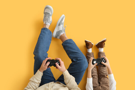 Father and his little son playing video games on yellow background, closeup