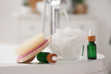 Massage brush with serum and loofah on bathtub, closeup