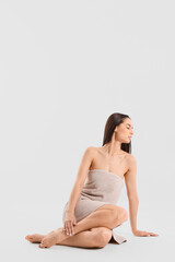 Obraz premium Beautiful woman in towel after shower sitting on light background
