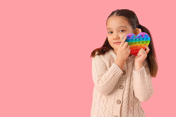 Little Asian girl with autistic disorder and pop it fidget toy on pink background
