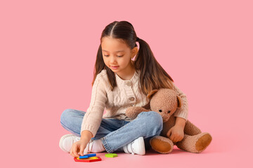 Little Asian girl with autistic disorder playing on pink background