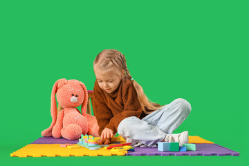 Little girl with autistic disorder playing on mat against green background