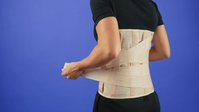 Woman in pain from back injury wearing lumbar brace corset on a blue background, copy space