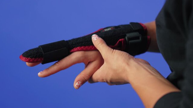 woman adjusting a splint on her middle finger, injured finger blue background