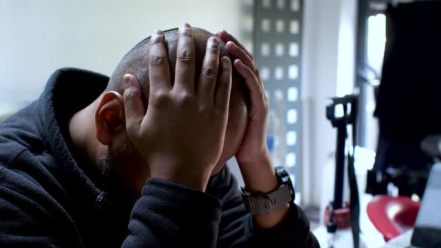 A man sits with his head cradled in his hands, his expression fraught with the weight of burdens, vividly capturing the palpable strain of stress and anxiety.