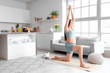 Sporty pregnant woman training on fitness mat in kitchen