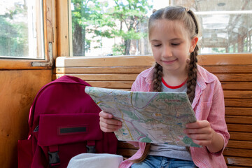 An 8-10-year-old girl, a traveler, rides in an old tram, looking at a map and sights. Vacation, travel, trip and summer is the concept of summer travel.