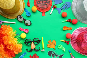 Frame made of hats, funny glasses and party decor on green background. April Fools Day celebration