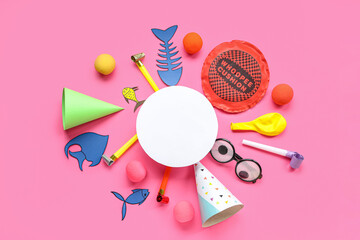 Blank card with paper fishes, whoopee cushion and party decor on pink background. April Fools Day celebration