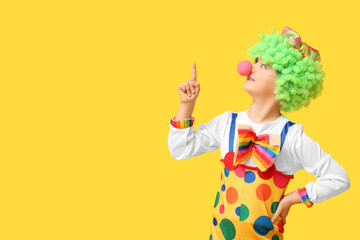 Funny little boy in clown costume with raised index finger on yellow background. April Fools Day...
