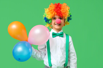 Funny little boy in clown wig with nose holding balloons on green background. April Fools Day celebration