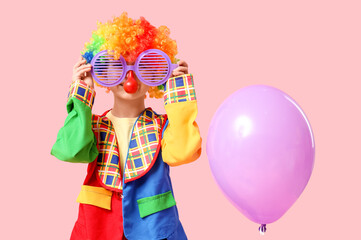 Cute little boy in clown costume with funny glasses and balloon on pink background. April Fools Day celebration