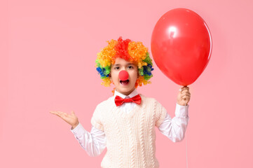 Surprised little boy in clown wig and nose holding balloon on pink background. April Fools Day celebration
