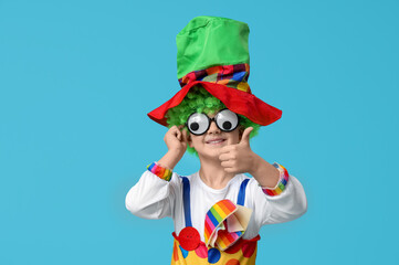 Cute little boy in clown costume with funny glasses showing thumb-up on blue background. April...