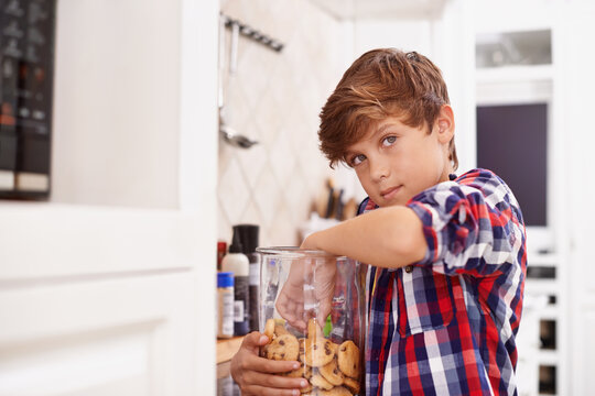 Eating, cookies and portrait of child in home with glass, container or sneaking with a jar of sweets. House, kitchen and kid craving a taste of sugar with biscuit addiction or snack on unhealthy food