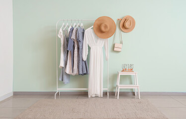 Rack of trendy clothes and hats near white wall