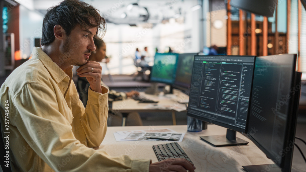 Fototapete Male Caucasian Game Programmer Coding On Desktop Computer In Game Design Studio Diverse Office. Focused Man Writes Lines Of Code, Does Gameplay Engineering For New Immersive 3D Survival Video Game.