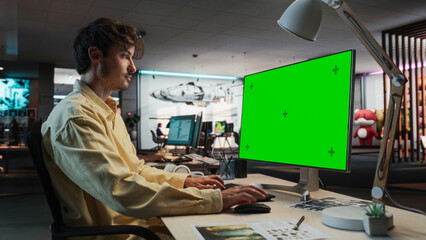 Caucasian Man Using Desktop Computer with Mock-up Green Screen Chromakey. Male Concept Artist Working in Game Design Startup Diverse Office, Creating Immersive Gameplay For New Survival Video Game.