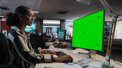 Portrait of Creative Black Female Sitting at a Desk Using Desktop Computer with Mock-up Green Screen. Female Concept Artist Working in Game Design Startup Office, Creating Immersive Gameplay. - obrazy, fototapety, plakaty