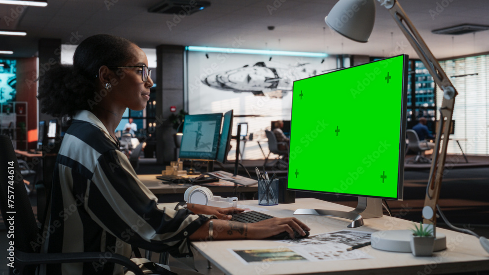 Poster Portrait of Creative Black Female Sitting at a Desk Using Desktop Computer with Mock-up Green Screen. Female Concept Artist Working in Game Design Startup Office, Creating Immersive Gameplay.