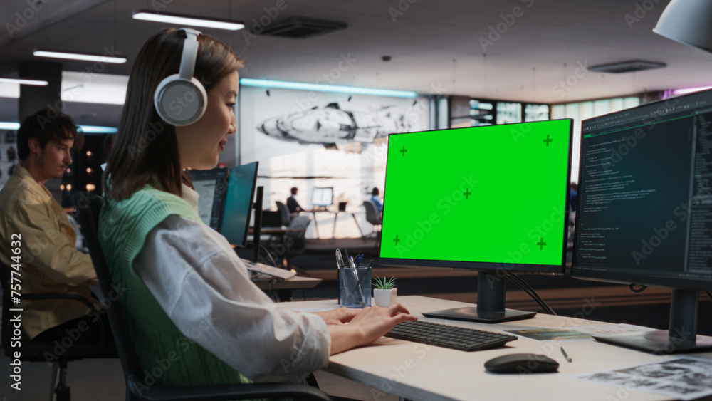 Leinwandbilder Female Asian Game Programmer Coding On Desktop Computer With Green Screen Chromakey On Display In Game Development Studio Office. Focused Woman Does Gameplay Engineering For New 3D RPG Video Game.