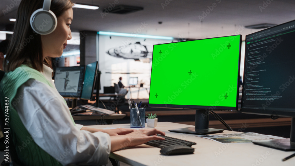 Poster Female Asian Game Programmer Coding On Desktop Computer With Green Screen Chromakey On Display In Game Development Studio Office. Focused Woman Does Gameplay Engineering For New 3D RPG Video Game.