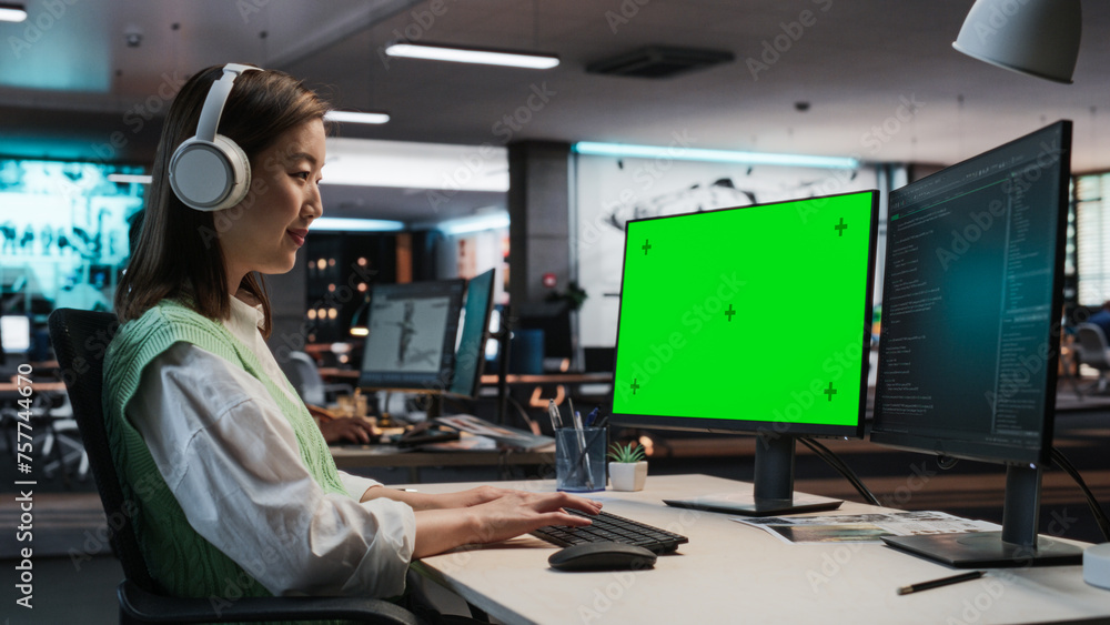 Aufkleber Female Asian Game Programmer Coding On Desktop Computer With Green Screen Chromakey On Display In Game Design Studio Office. Focused Woman Does Gameplay Engineering For New Immersive 3D RPG Video Game