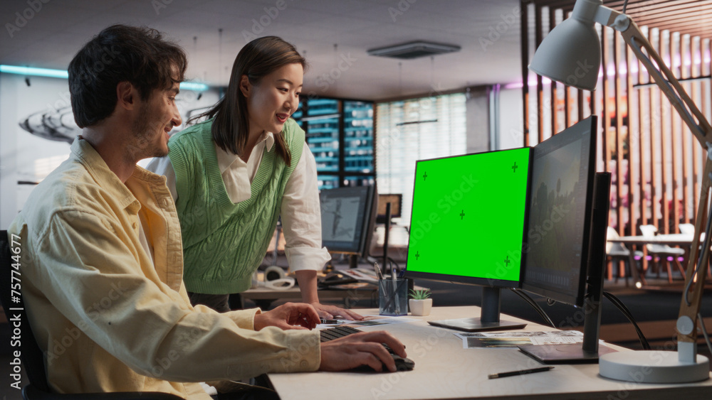 Poster Caucasian Male Game Designer Using Desktop Computer With Green Screen And Talking to Asian Female Project Manager in Game Development Studio Office. Diverse Colleagues Discussing New RPG Game