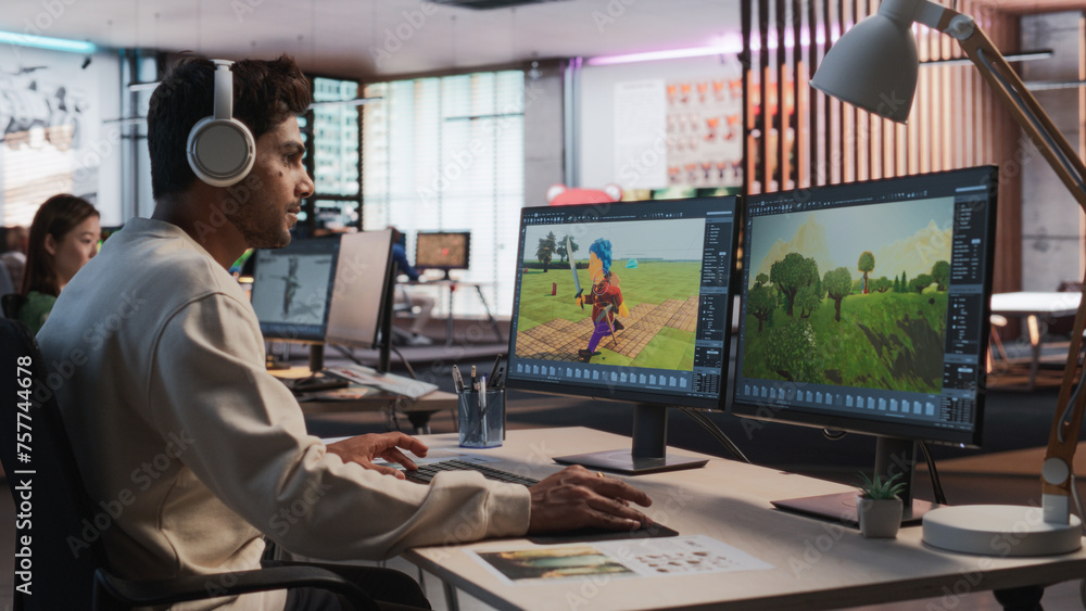 Poster Indian Male Game Designer Using Desktop Computer With 3D modelling Software To Design Characters And World For Immersive Adventure Video Game. Man Working In Game Development Company Diverse Office.