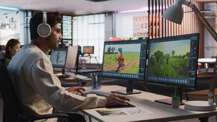 Indian Male Game Designer Using Desktop Computer With 3D modelling Software To Design Characters And World For Immersive Adventure Video Game. Man Working In Game Development Company Diverse Office.
