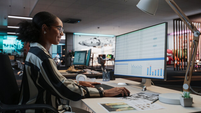 African Female Manager Using Desktop Computer With Analytics Software wth Financial Reports. Woman Working In Game Development Company Diverse Office
