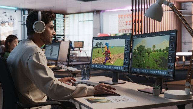 Indian Male Game Designer Using Desktop Computer With 3D modelling Software To Design Characters And World For Immersive Adventure Video Game. Man Working In Game Development Company Diverse Office.