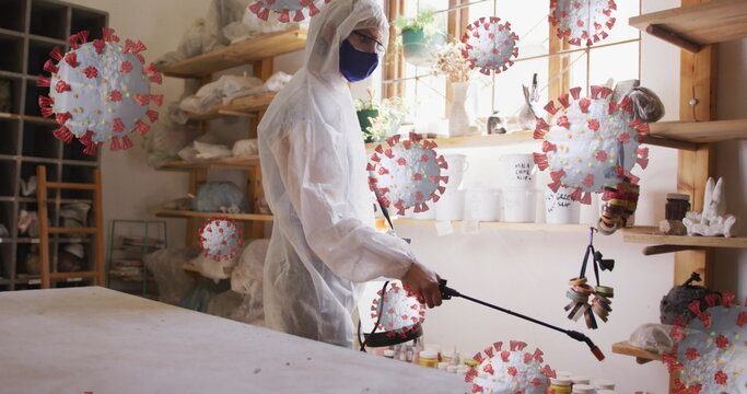 Image of virus cells over caucasian man with face mask and safety suit disinfecting