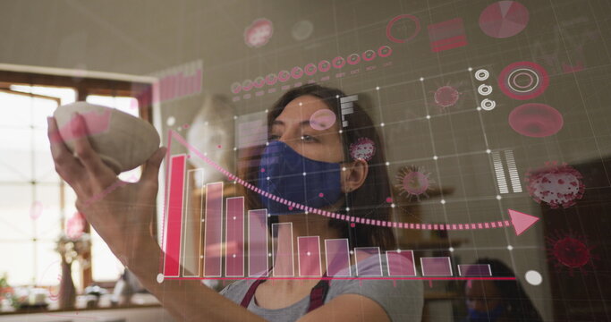 Image of covid 19 cells and statistics over woman working in pottery studio wearing face mask - Powered by Adobe