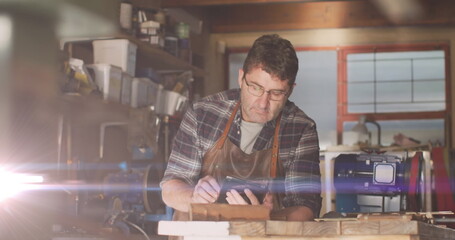 Image of glowing light over caucasian man using tablet in workshop