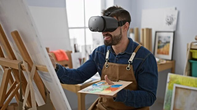 Confident bearded young hispanic man artist smiling while drawing indoors using virtual reality glasses in a futuristic art studio class.