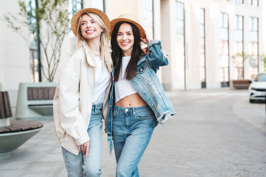 Two young beautiful smiling hipster female in trendy summer clothes. Carefree women posing in the street. Positive models having fun outdoors at sunny day. Cheerful and happy. In hat