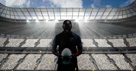 Golden confetti falling over silhouette of male rugby player against sports stadium