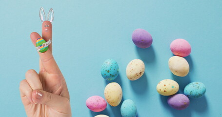 Image of hand with easter decorations and easter eggs over blue background