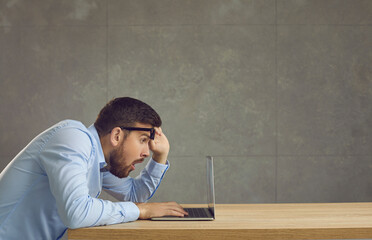 Side view of amazed shocked man with a confused expression looking at a laptop screen from under...