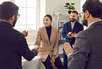 Team leader handshaking happy surprised female employee in office. Colleagues supporting applauding...