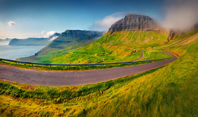 Asphalt road to Sydradalur village. Wonderful summer view of Faroe Islands. Splendid morning scene...