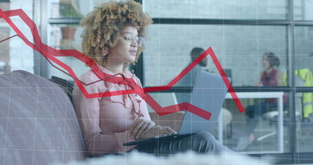 Red graph processing over biracial casual businesswoman using laptop in office lounge