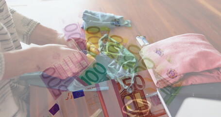 Image of Euro bills lying on a table over Caucasian woman sewing face masks