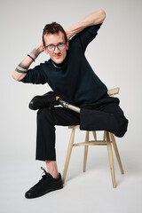 Studio portrait of a successful happy tattooed one legged disabled young male amputee with prosthetic leg wearing casual dark blue clothing. 