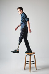 Studio portrait of a successful happy tattooed one legged disabled young male amputee with prosthetic leg wearing casual dark blue clothing. 